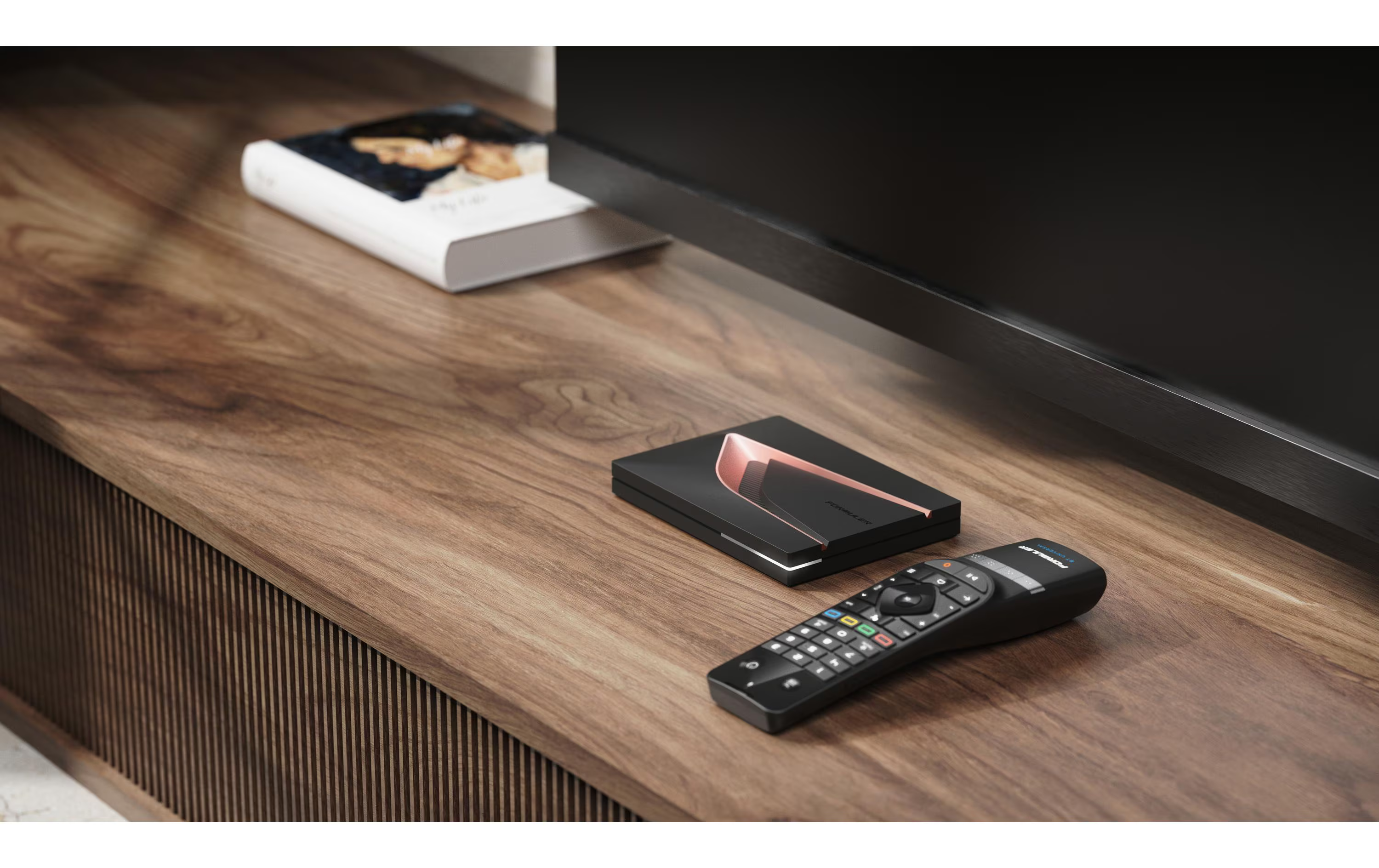 Télécommande noire et appareil noir avec accent de cuivre sur table en bois à côté d'un livre.