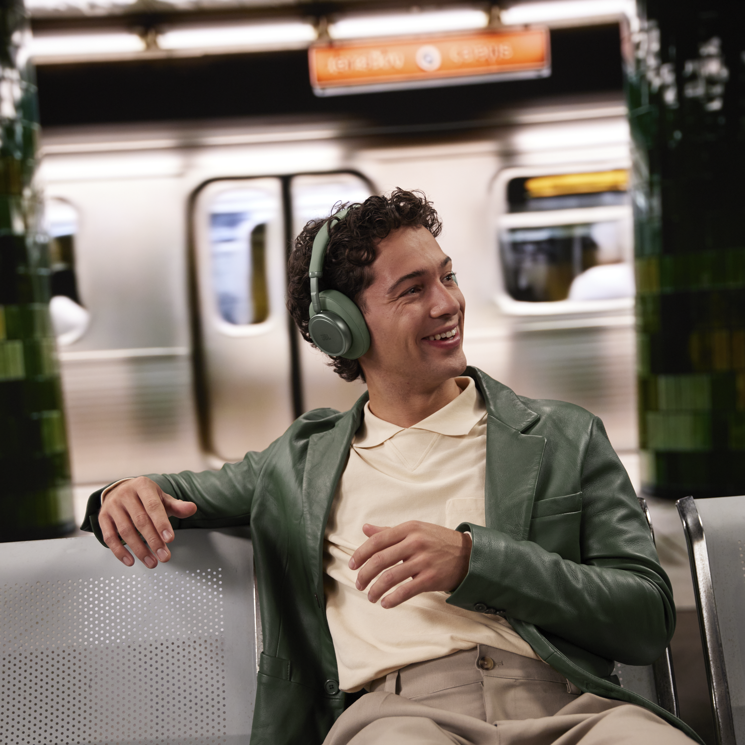 Un homme portant un casque est assis dans une zone d'attente de métro, avec un train en arrière-plan.