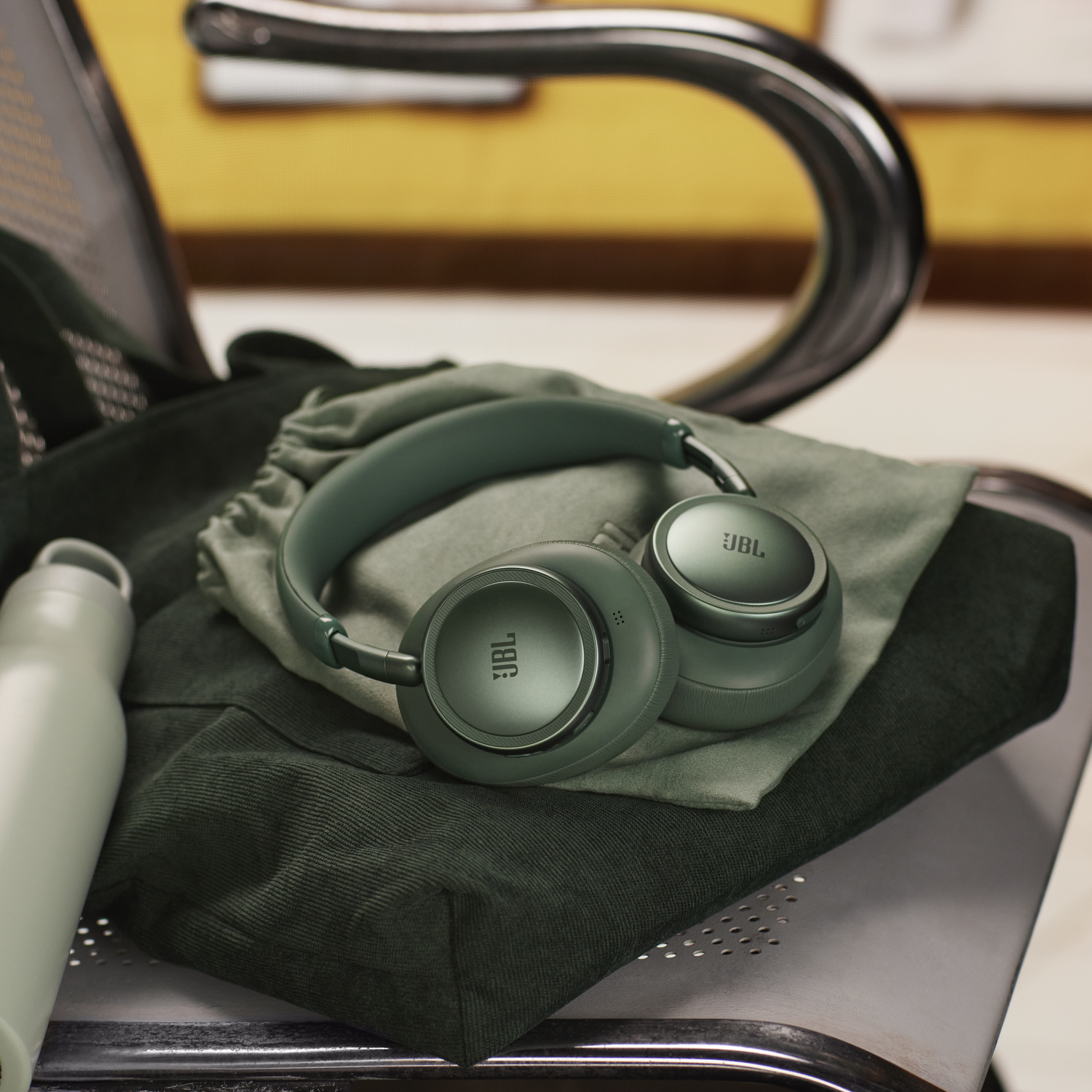 Casque JBL vert posé sur des vêtements pliés à côté d'une bouteille d'eau.