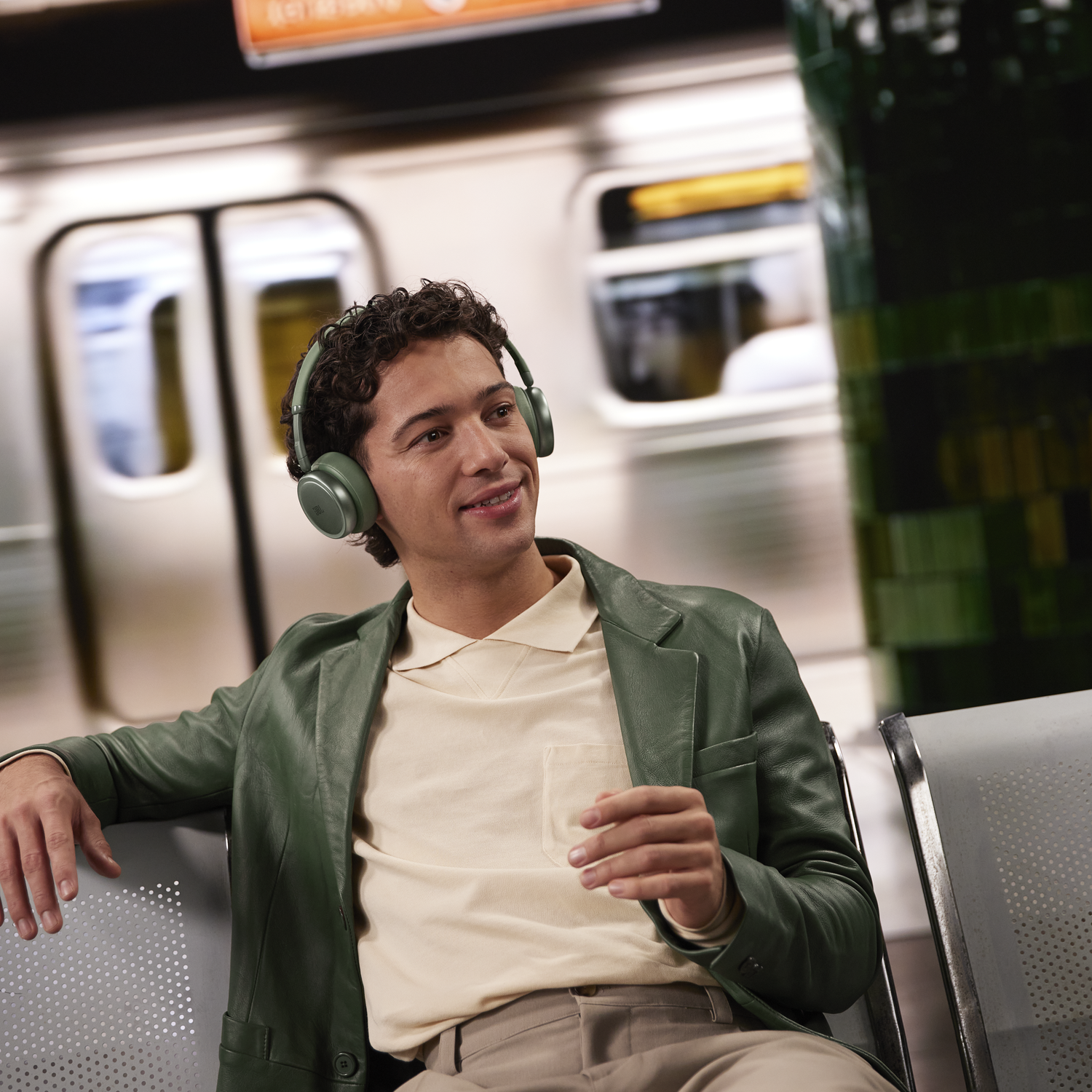 A man wearing headphones sits on a bench in a subway station.