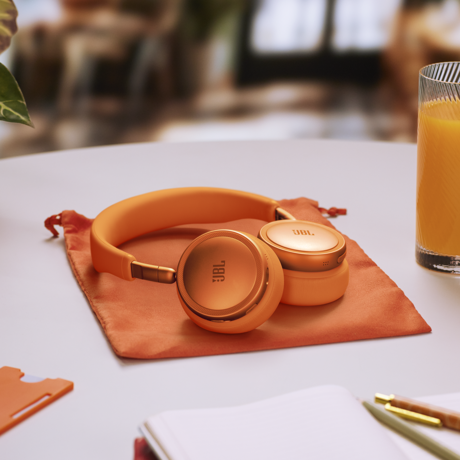 Orange headphones on a pouch, next to a glass of juice and a notebook.