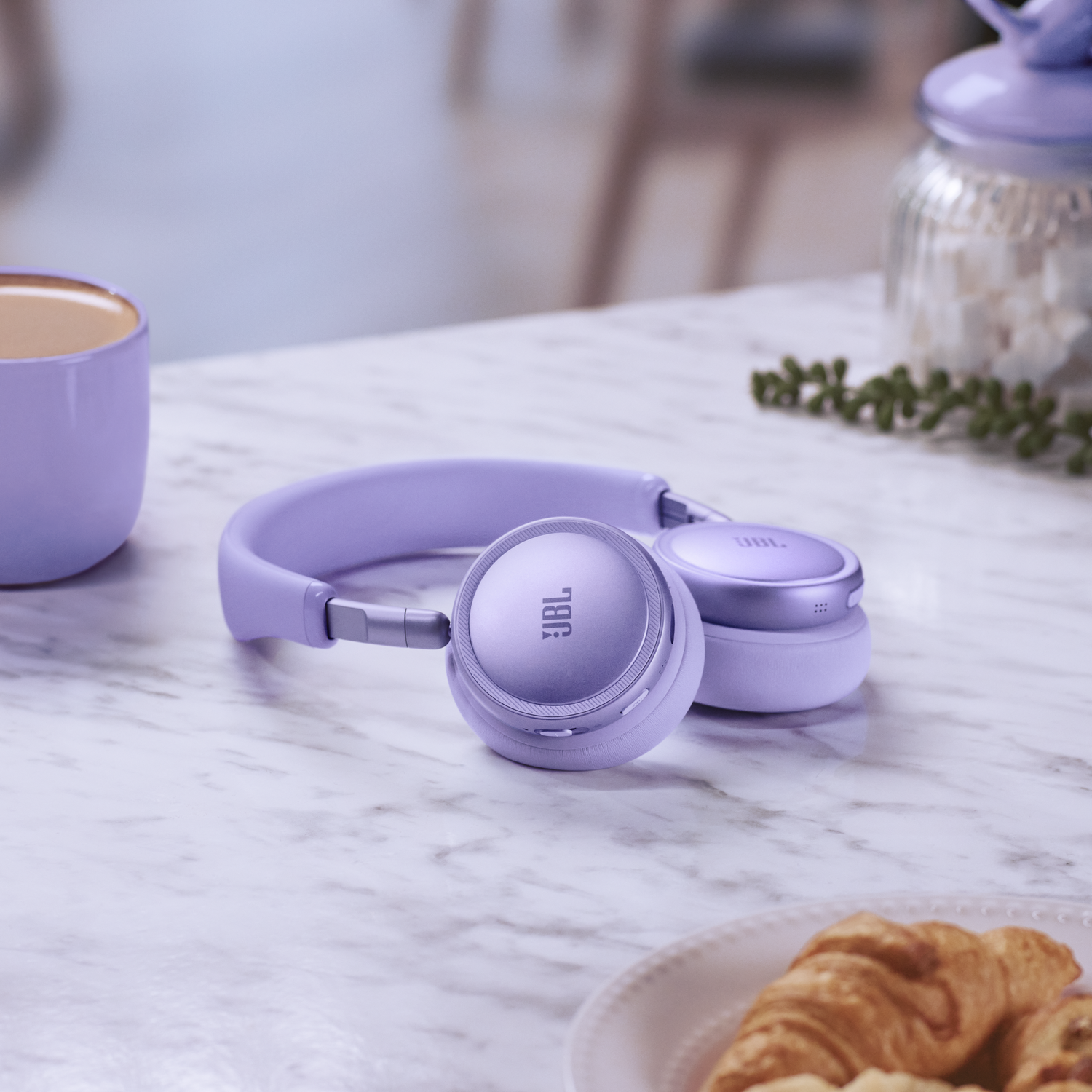 Light purple JBL headphones on a marble table with coffee and pastries.