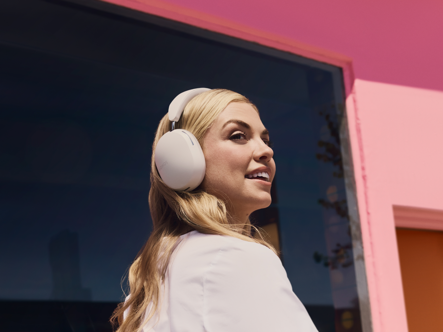 Una mujer rubia lleva auriculares blancos y mira hacia la derecha.