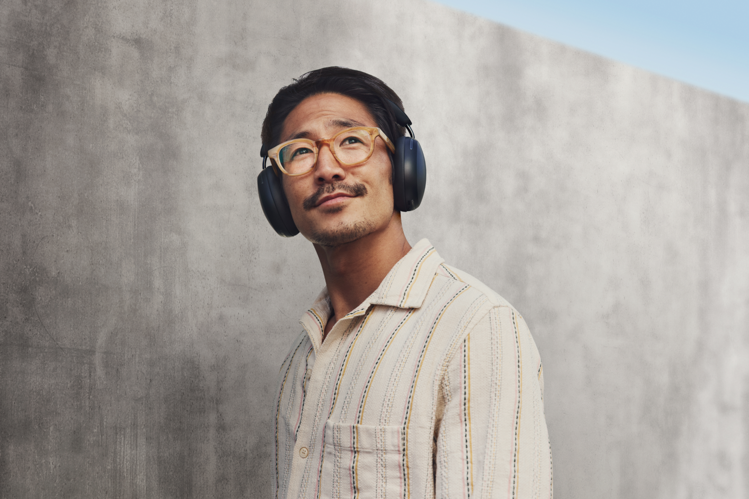 Hombre con gafas y auriculares frente a una pared de hormigón.