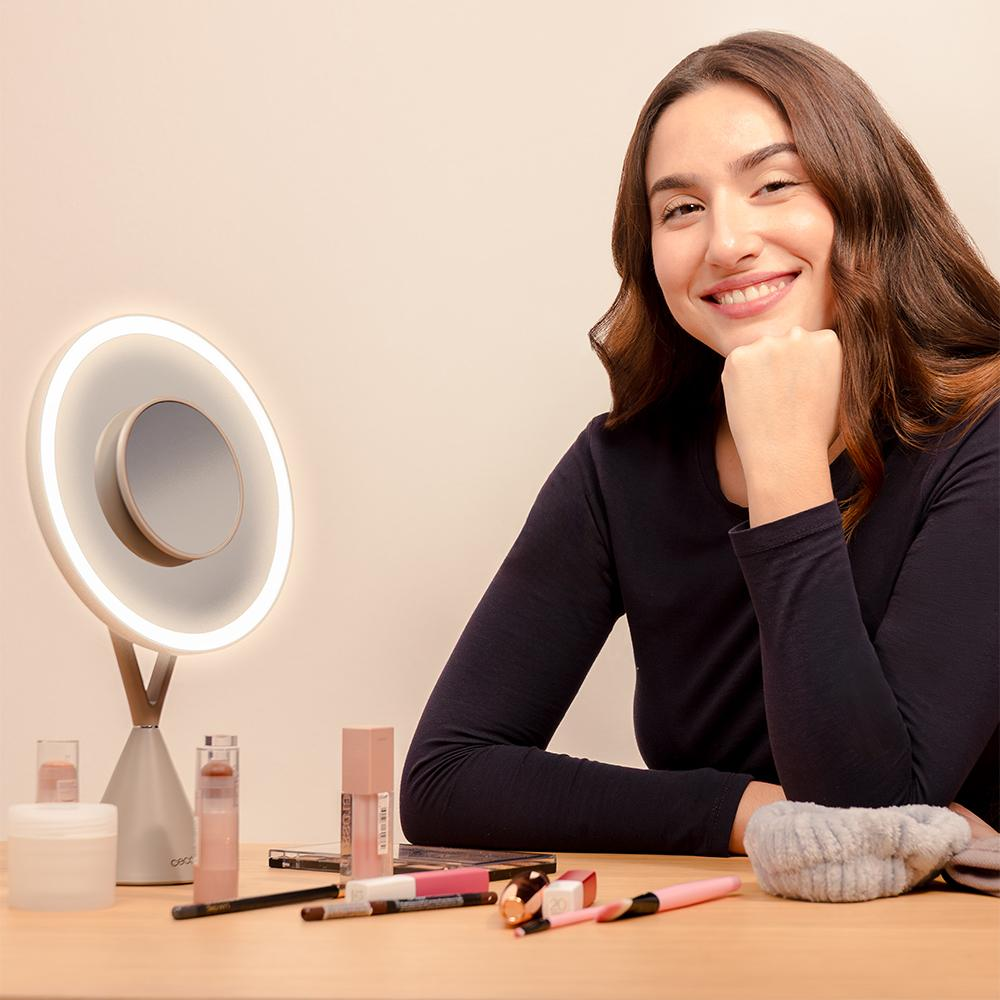 Mujer sonriente en tocador con maquillaje, luz de anillo y espejo.