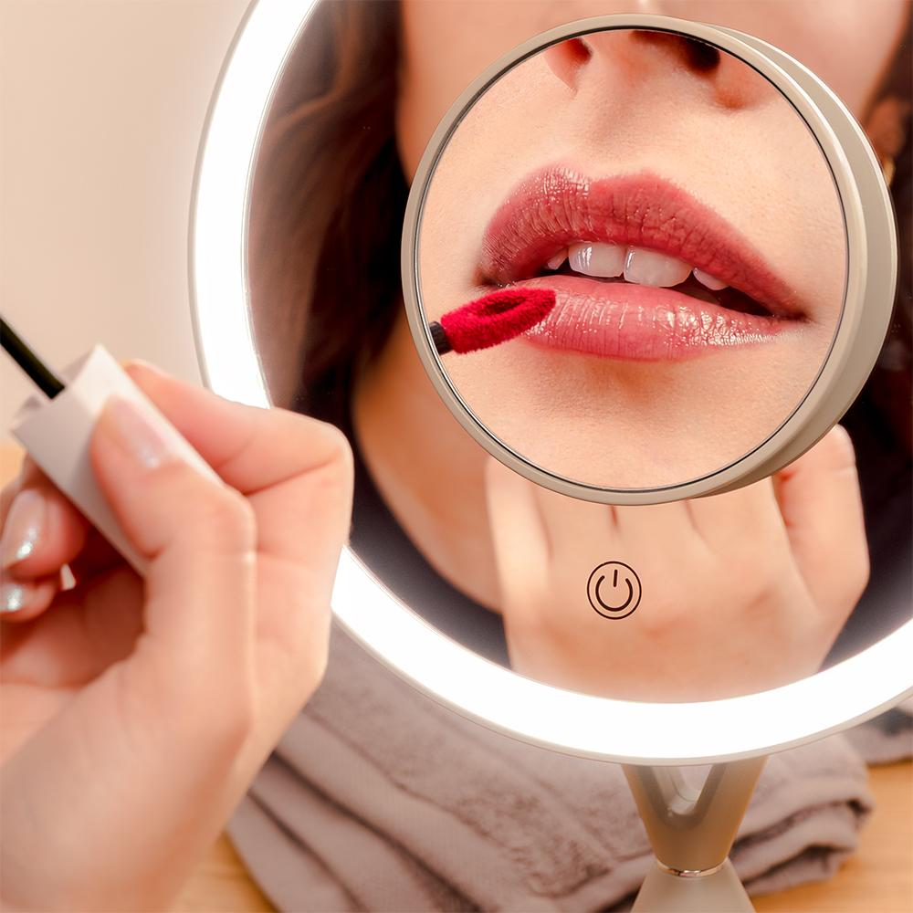 Mujer se aplica lápiz labial con aplicador rojo frente a espejo iluminado.