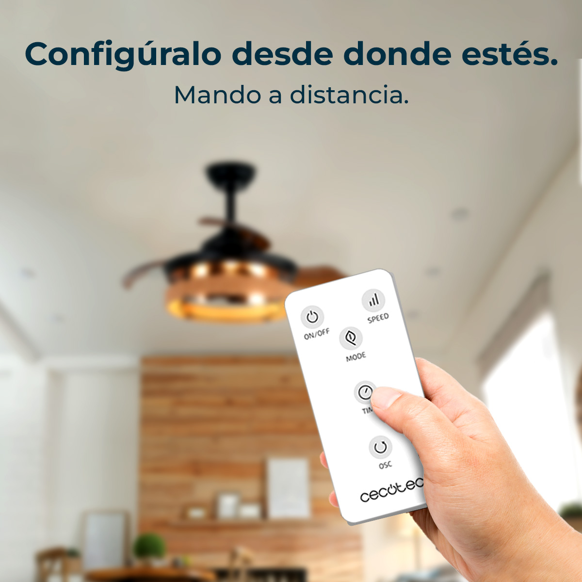 Una mano sostiene un mando a distancia frente a un ventilador de techo. El mando controla el ventilador.