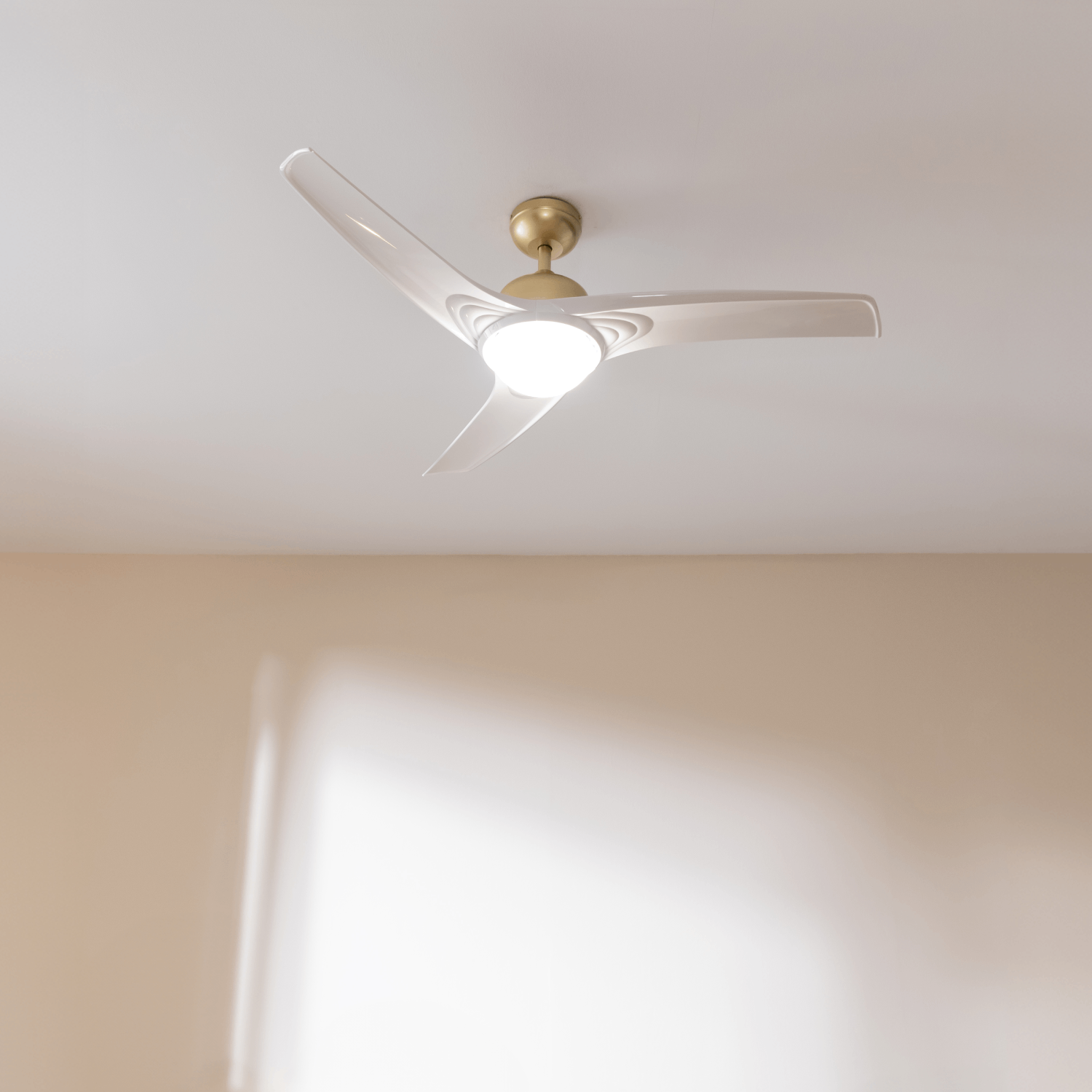 Un ventilador de techo moderno con tres aspas translúcidas y un soporte dorado.