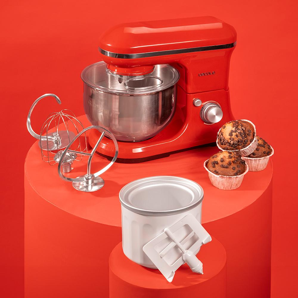 Batidora roja con accesorios y muffins de chocolate sobre fondo rojo.