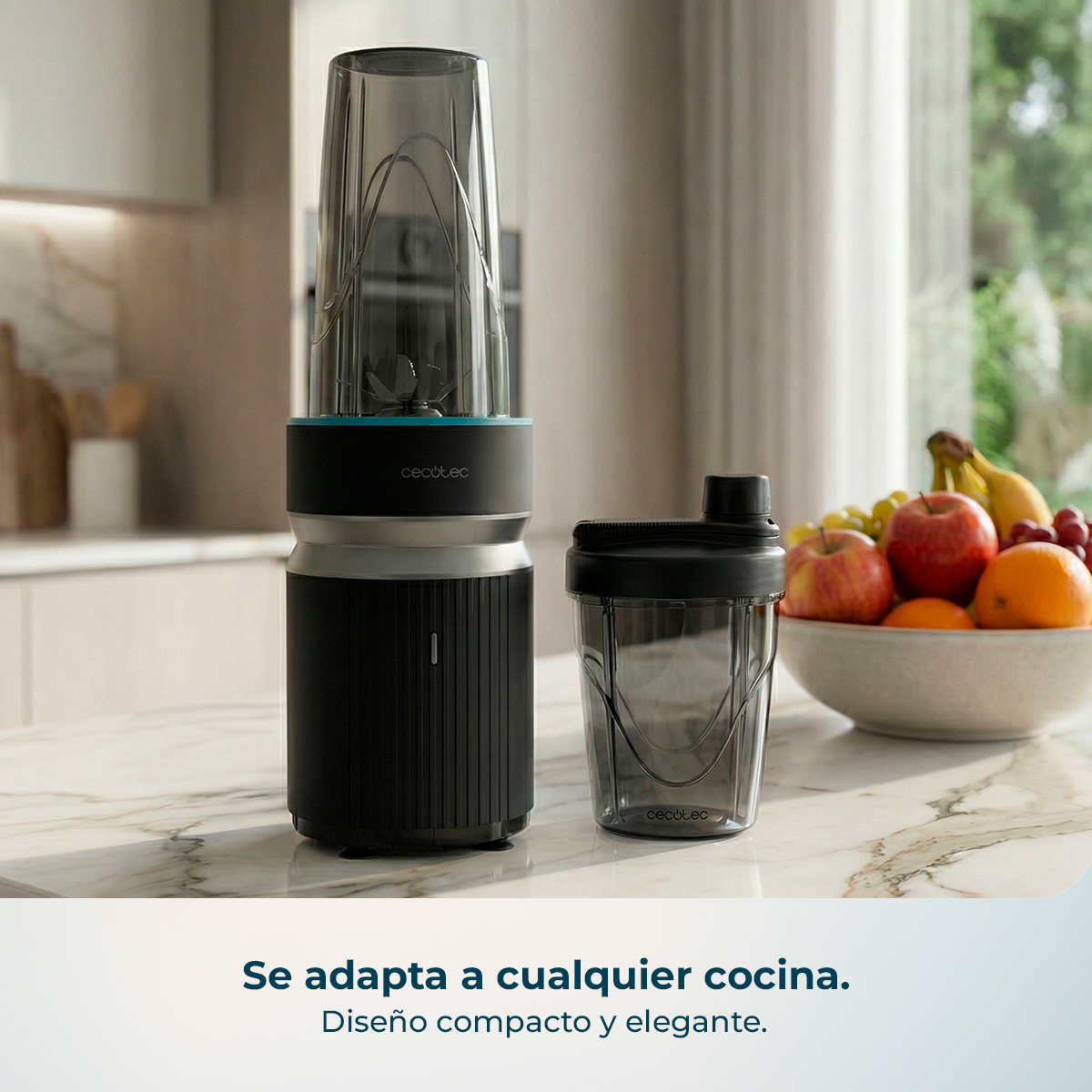 Batidora negra con vaso, cuenco de frutas al lado en encimera de mármol.