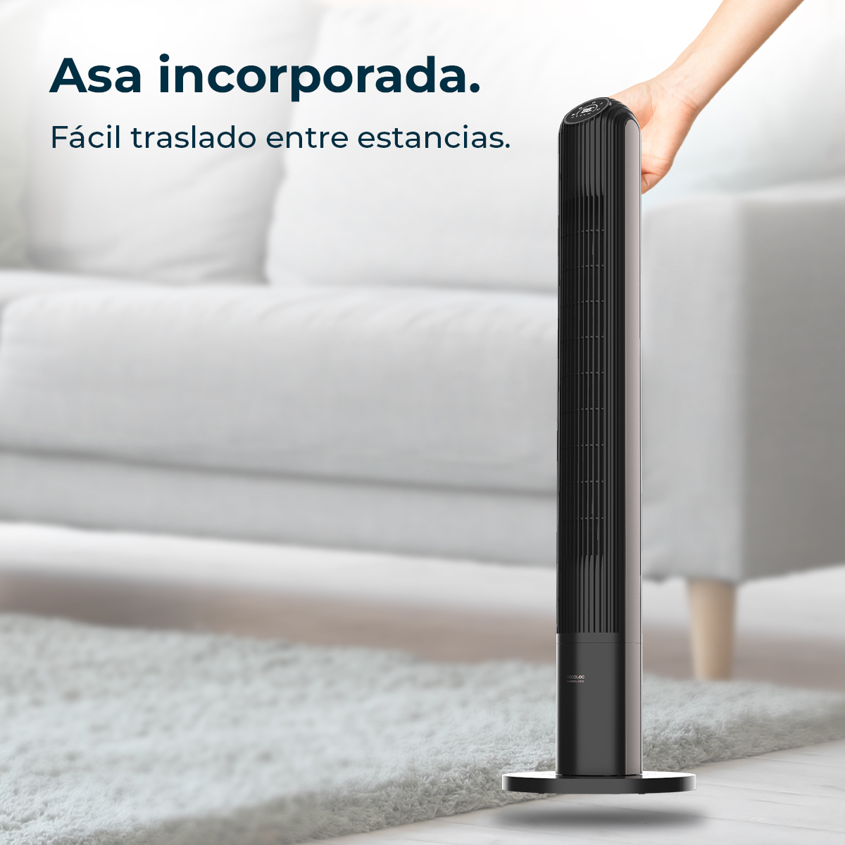 Un ventilador de torre negro y delgado sobre una alfombra frente a un sofá blanco.