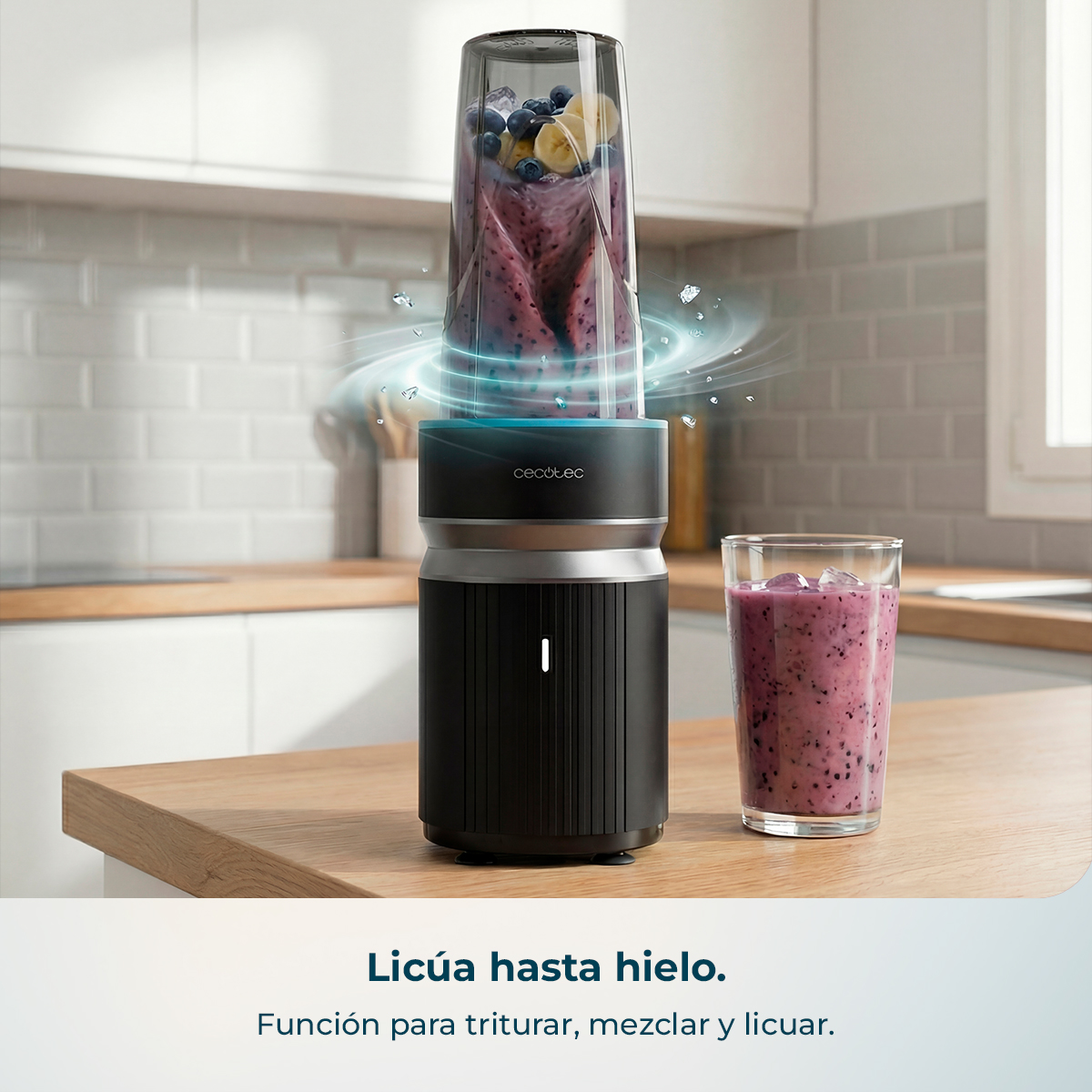 Una batidora negra con un vaso de batido y cubitos de hielo al lado sobre una mesa de madera.