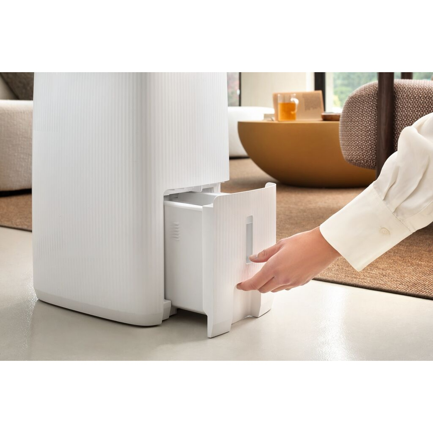 Una mano tira un cassetto bianco da un elettrodomestico bianco in un salotto.
