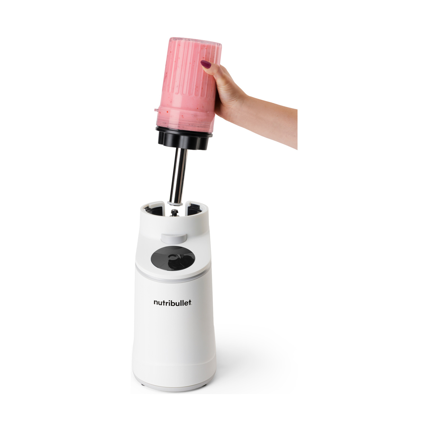 Una mano tiene una tazza con frullato rosa sopra un frullatore Nutribullet bianco.