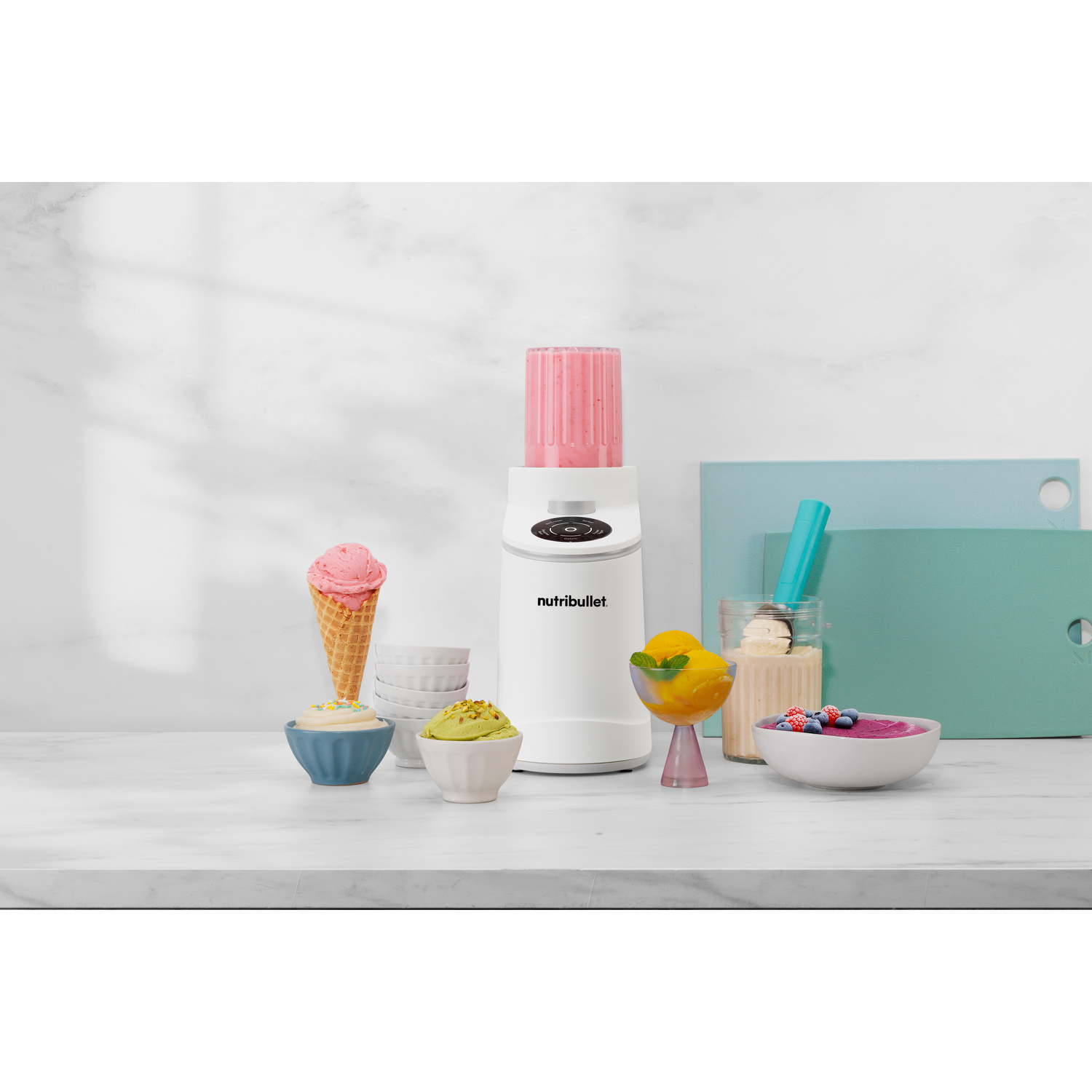 Un frullatore Nutribullet bianco con liquido rosa e vari dessert.