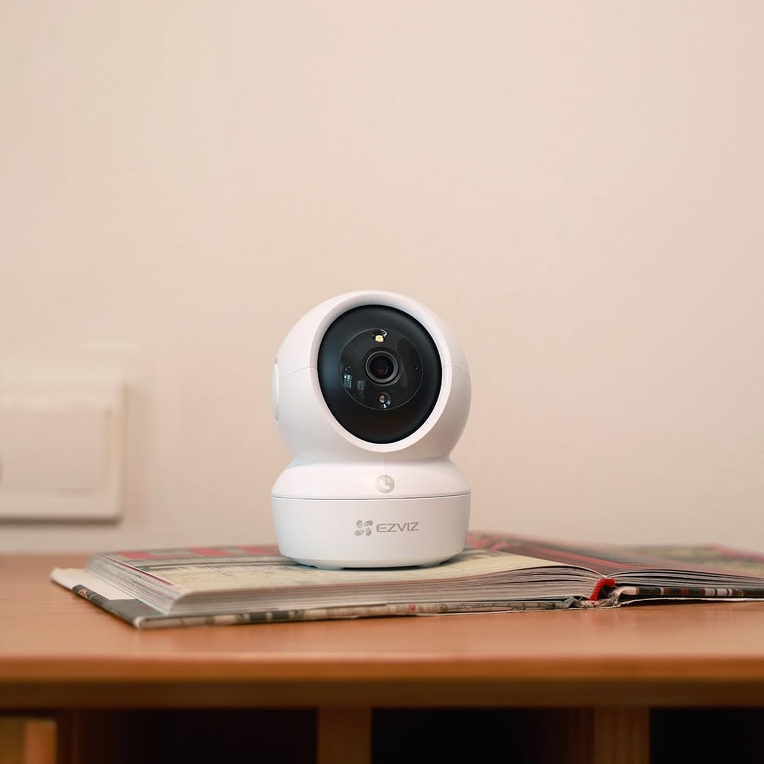 Una telecamera smart home di sorveglianza EZVIZ bianca, pan/tilt, su un libro.