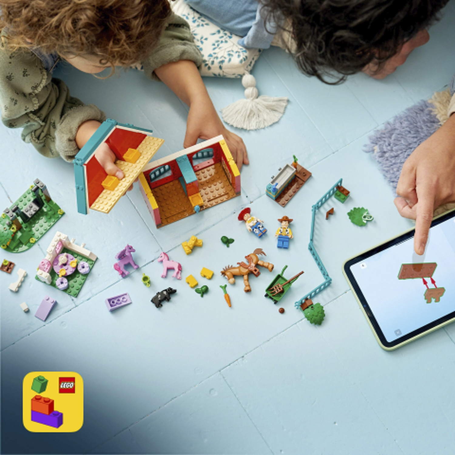 Bambini costruiscono scena fattoria Lego con cavalli, unicorni e figure, guidati da tablet.
