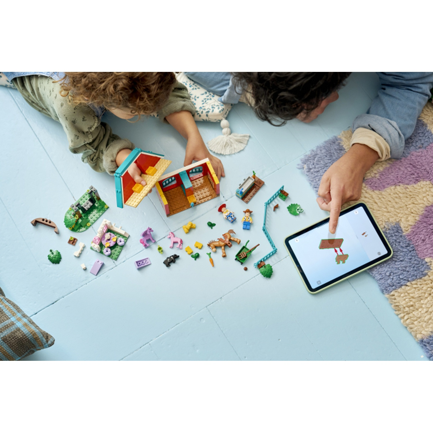 Due bambini costruiscono un set di fattoria Lego, guidati da un tablet, con animali e piante giocattolo.