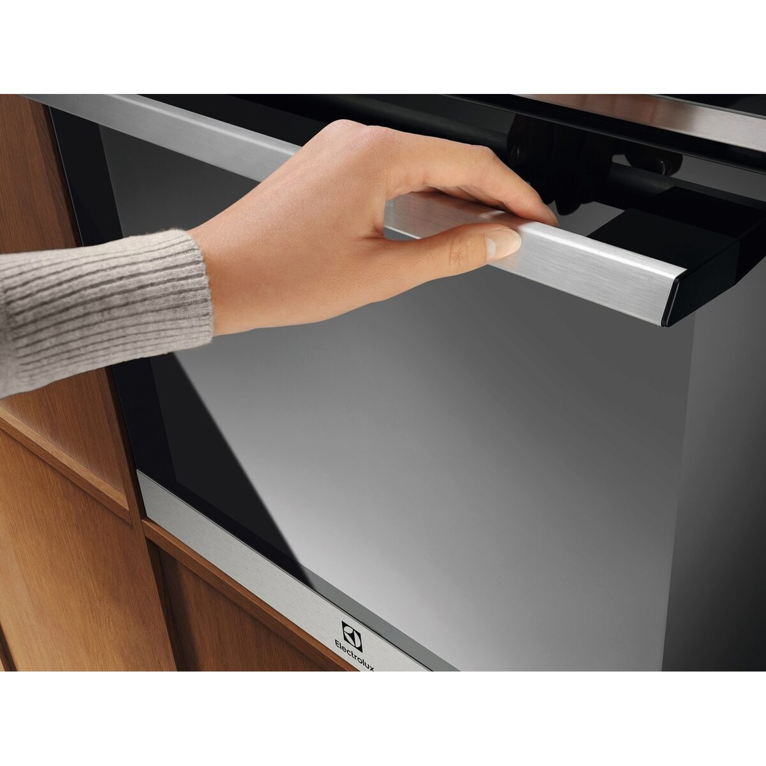 Una mano con un maglione grigio apre l'elegante maniglia di un forno moderno.