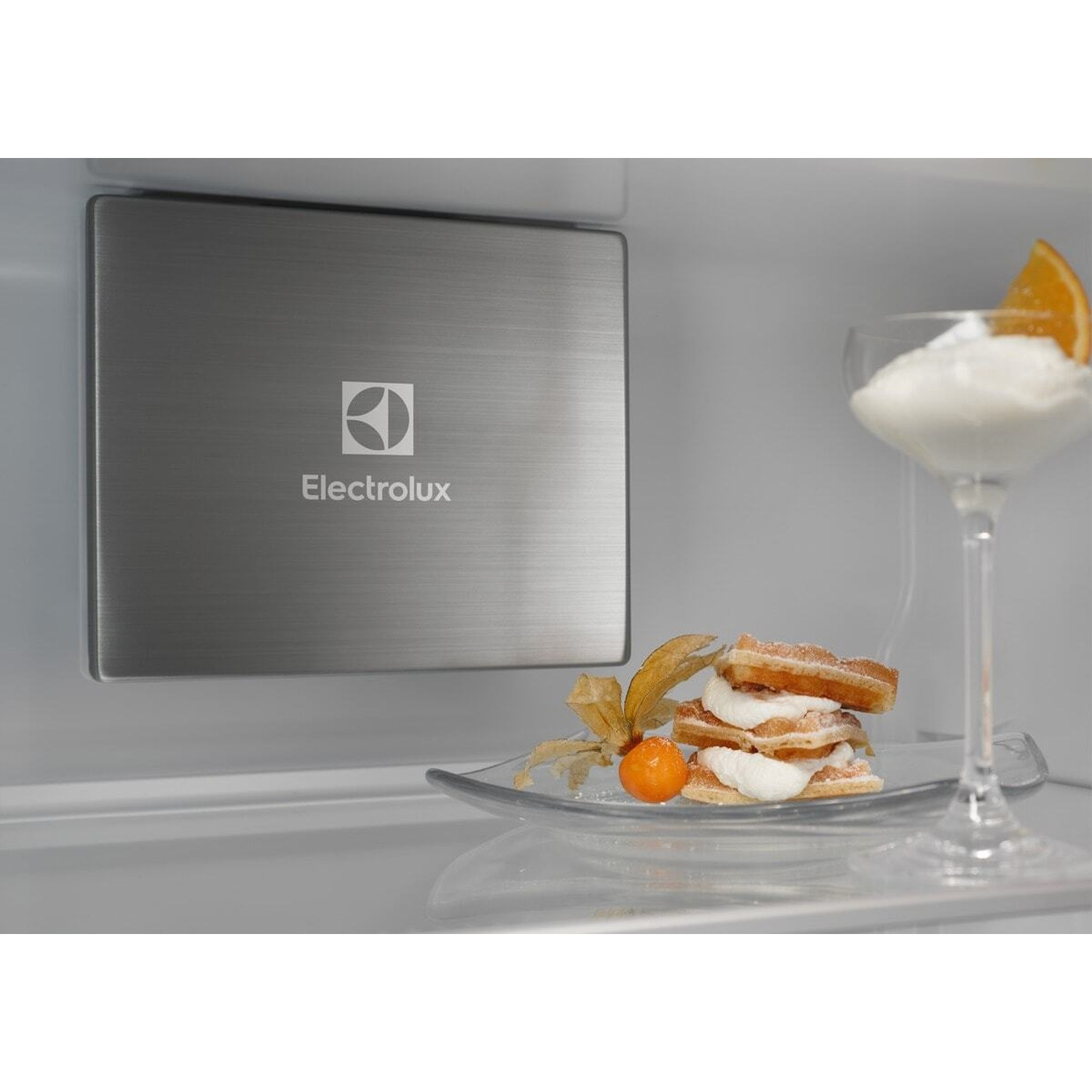 Logo Electrolux su piastra metallica accanto a waffle con panna e arancia in bicchiere.