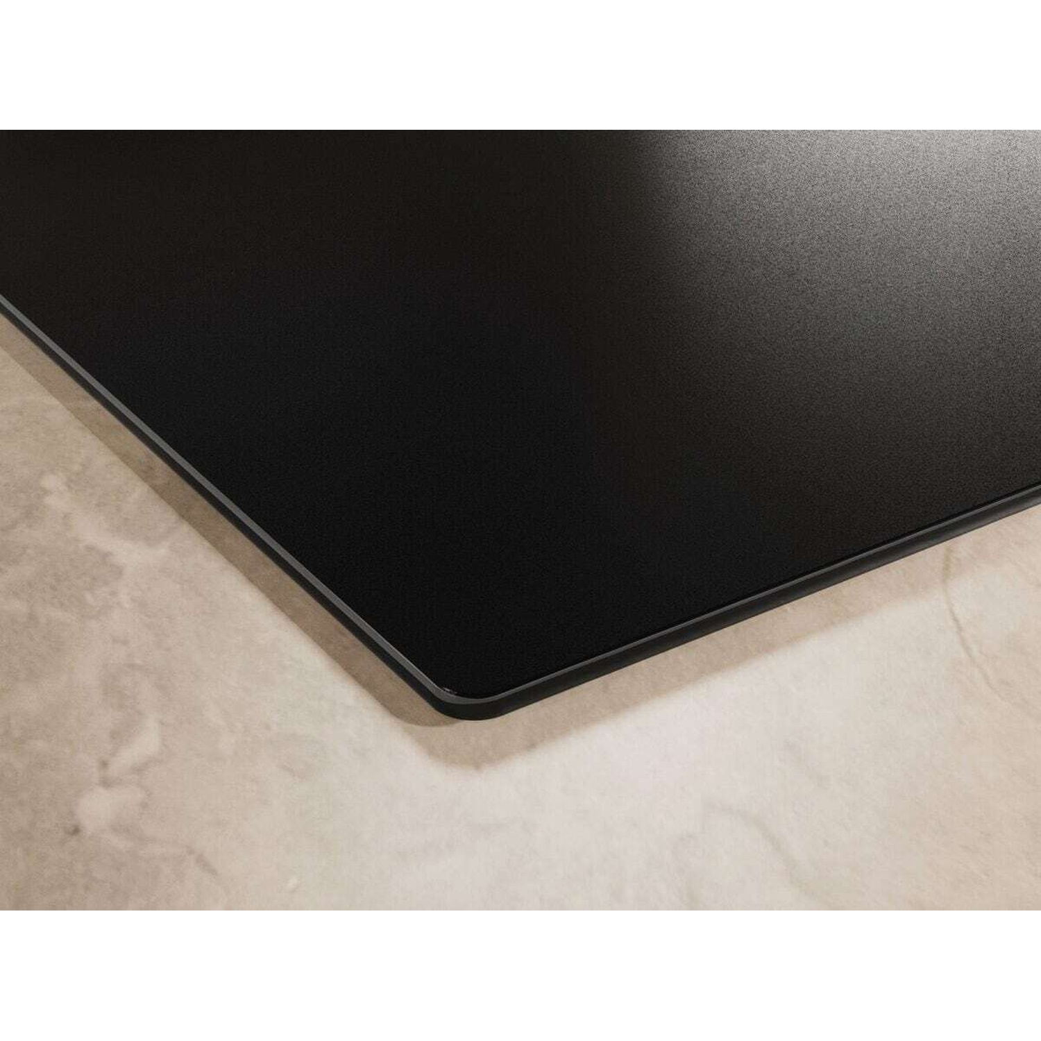 Primo piano di una superficie liscia e nera con un sottile bordo metallico su una superficie chiara e marmorizzata.