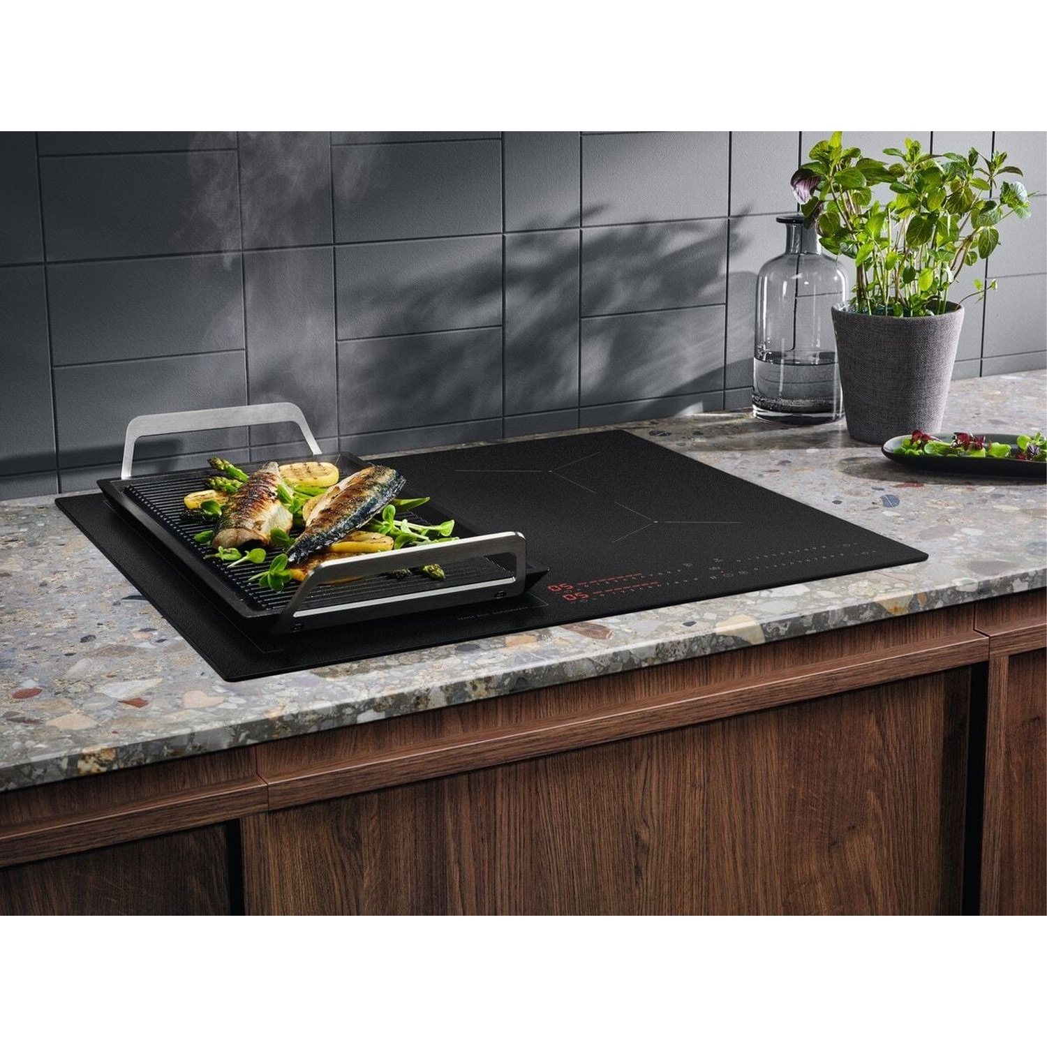 Piano cottura a induzione moderno con padella grill che cuoce pesce e verdure.