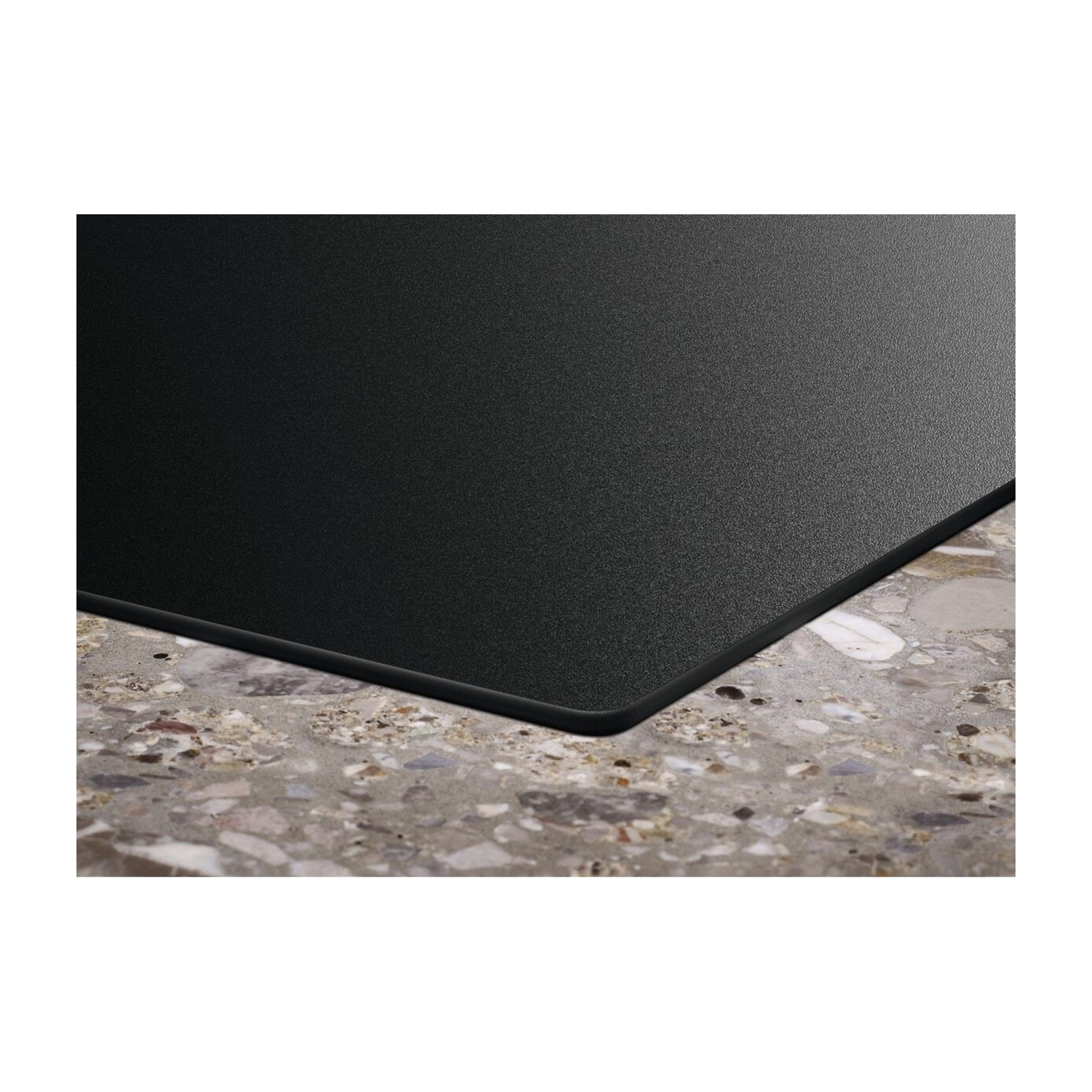 Un piano cottura nero poggia su un piano di lavoro in terrazzo con schegge di pietra grigie e beige.