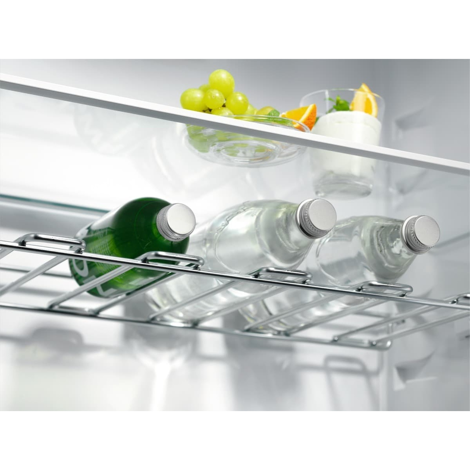 Tre bottiglie d'acqua su uno scaffale, con uva e yogurt sullo sfondo.
