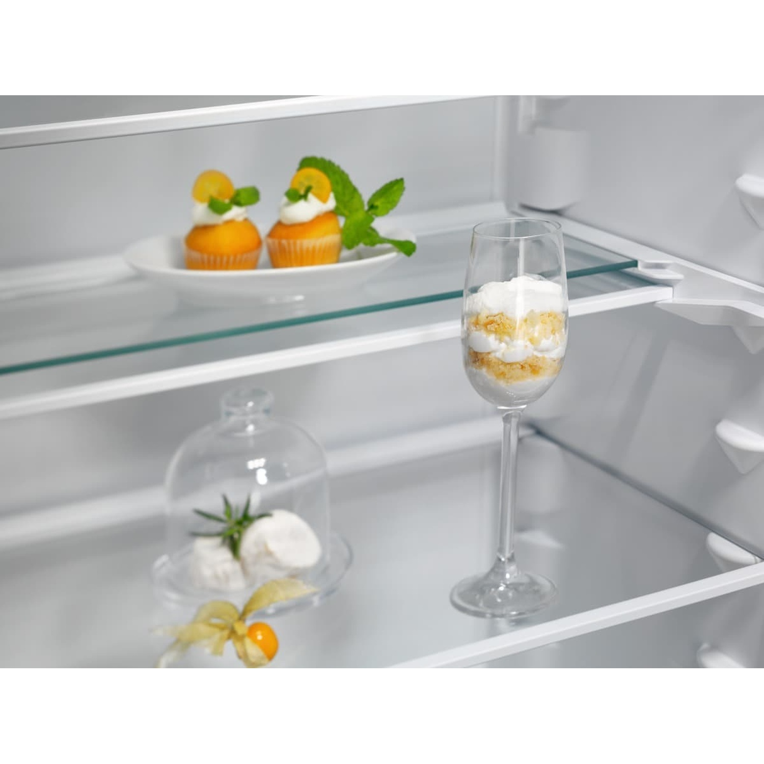 Due cupcake, un dessert in un bicchiere e palline di formaggio sotto una campana di vetro.