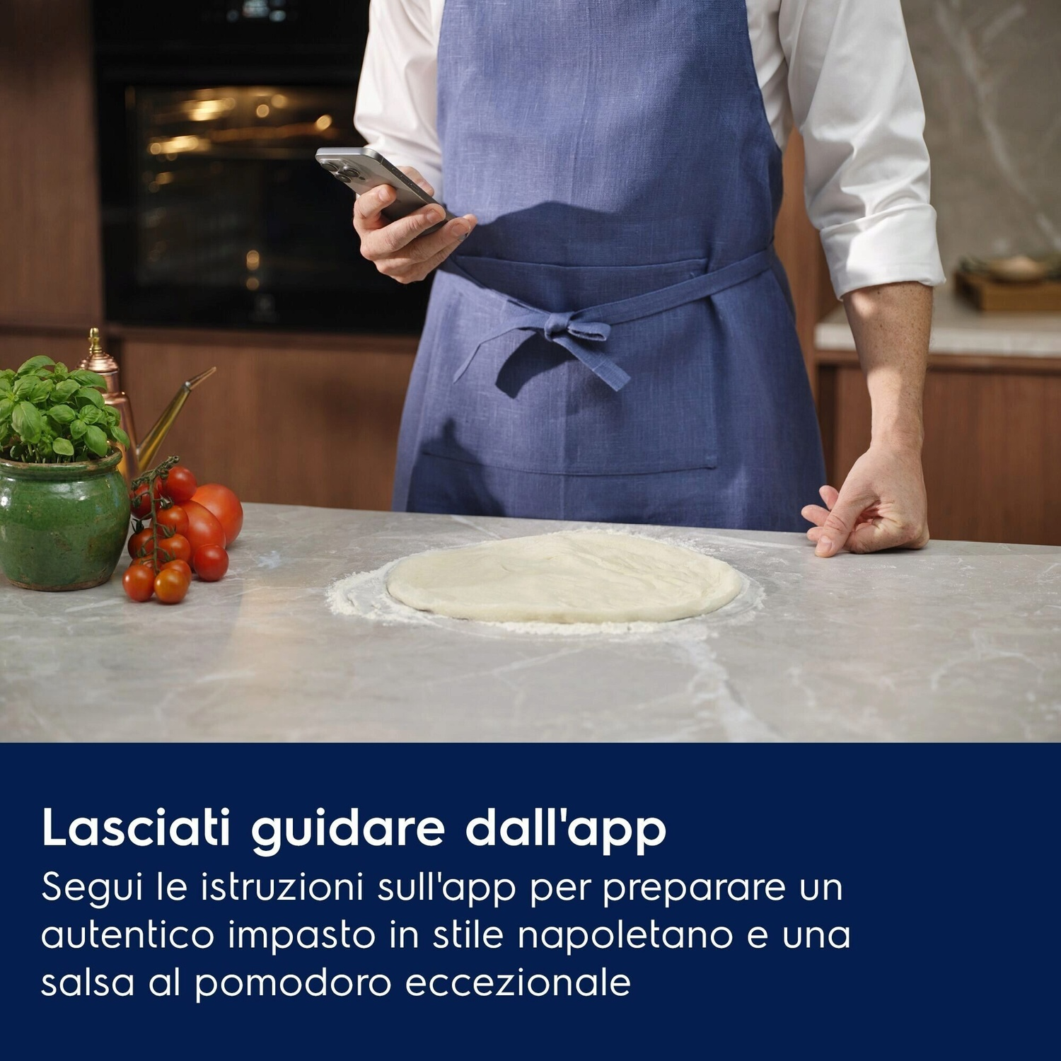 Uomo con smartphone e grembiule prepara impasto. Pomodori e basilico vicini.