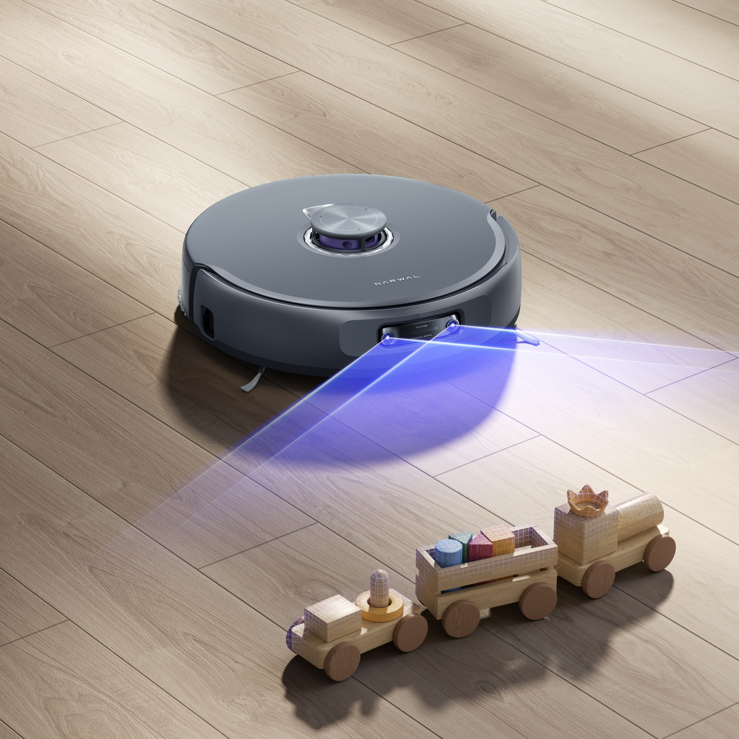 Un robot aspirapolvere grigio pulisce un pavimento in legno, aggirando un trenino di legno.