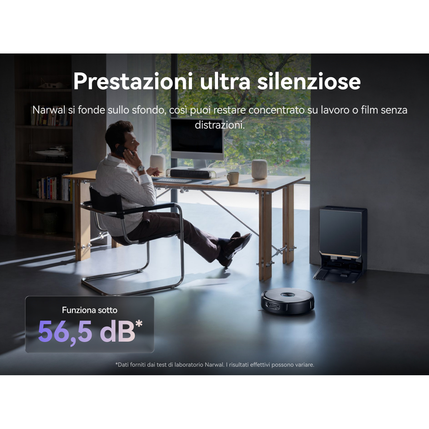 Uomo al telefono alla scrivania, robot aspirapolvere lavora silenziosamente.