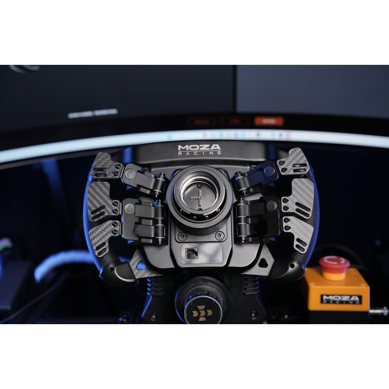 Un volante Moza Racing nero con accenti in fibra di carbonio e un dispositivo a pulsante rosso/arancio.