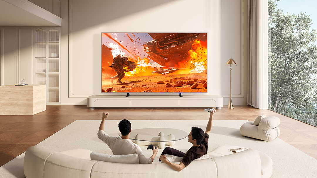 Két férfi videójátékot játszik egy modern nappaliban, robbanásokkal a képernyőn.
