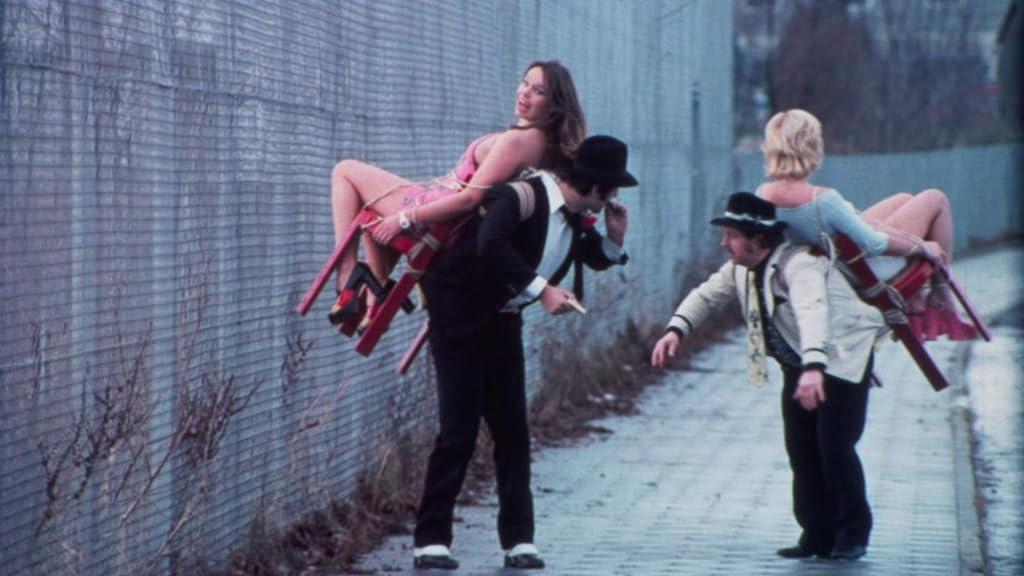Zwei Männer tragen Frauen auf Stühlen, die auf ihren Rücken befestigt sind.