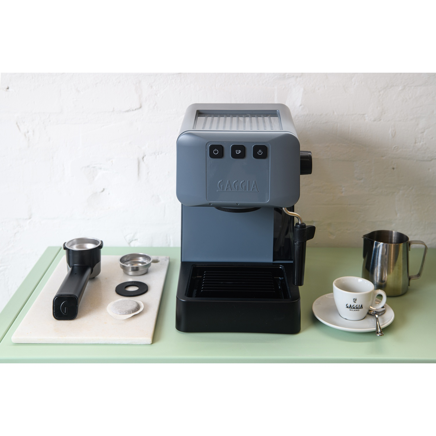 Una macchina per caffè espresso Gaggia grigia con portafiltro, capsula e tazza.