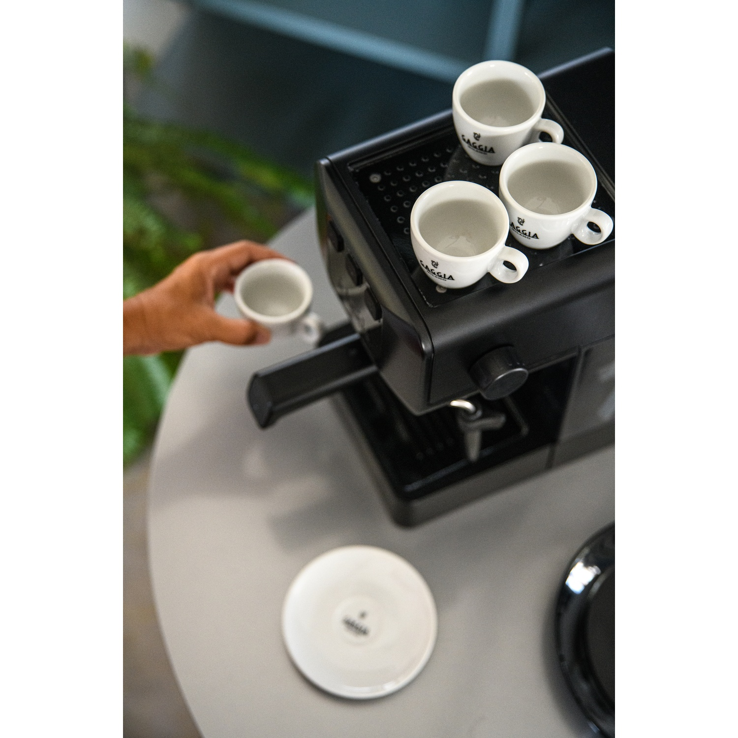 Una mano tiene una tazzina da espresso accanto a una macchina da caffè con tre tazze.