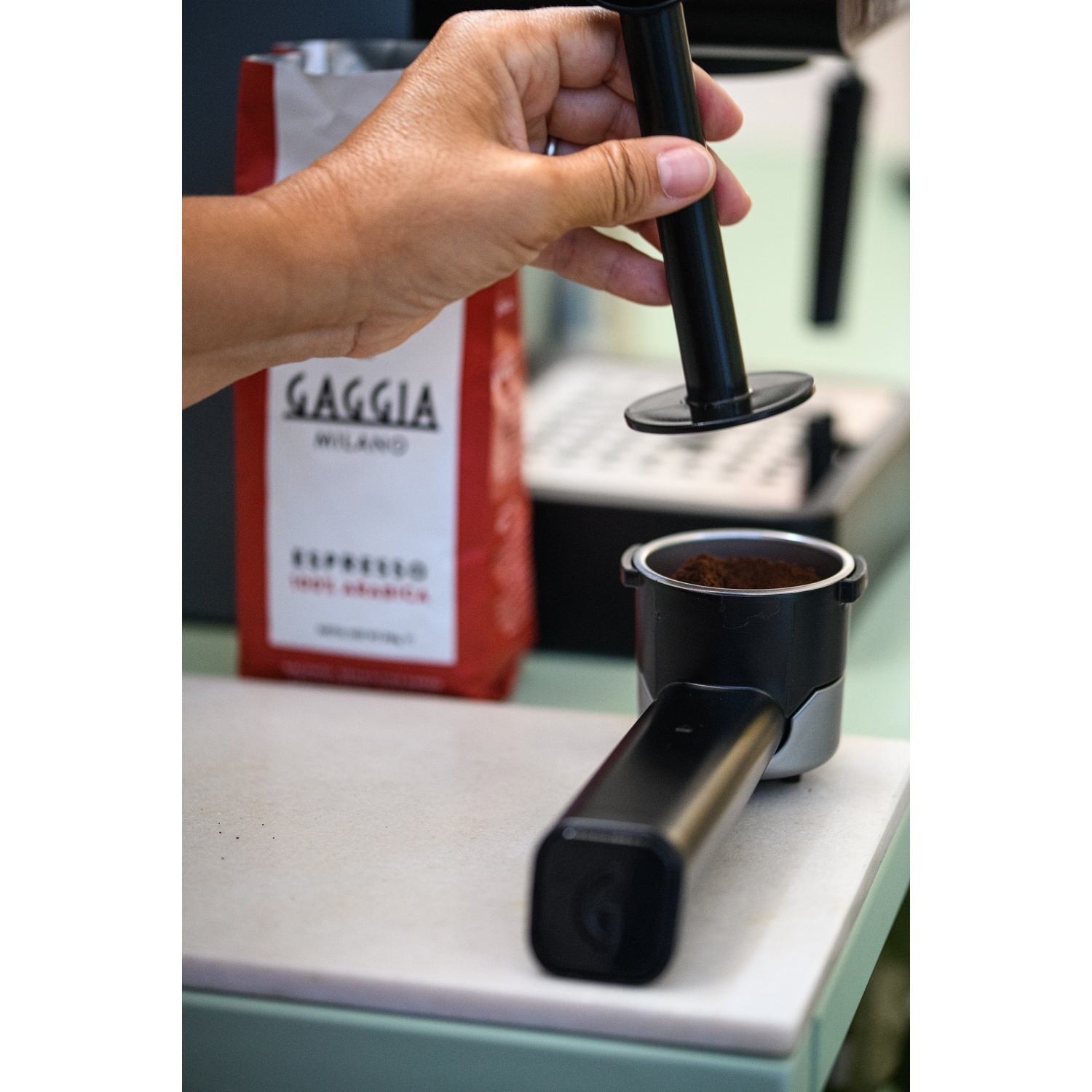 Una mano tiene un pressino su un portafiltro pieno di caffè macinato.