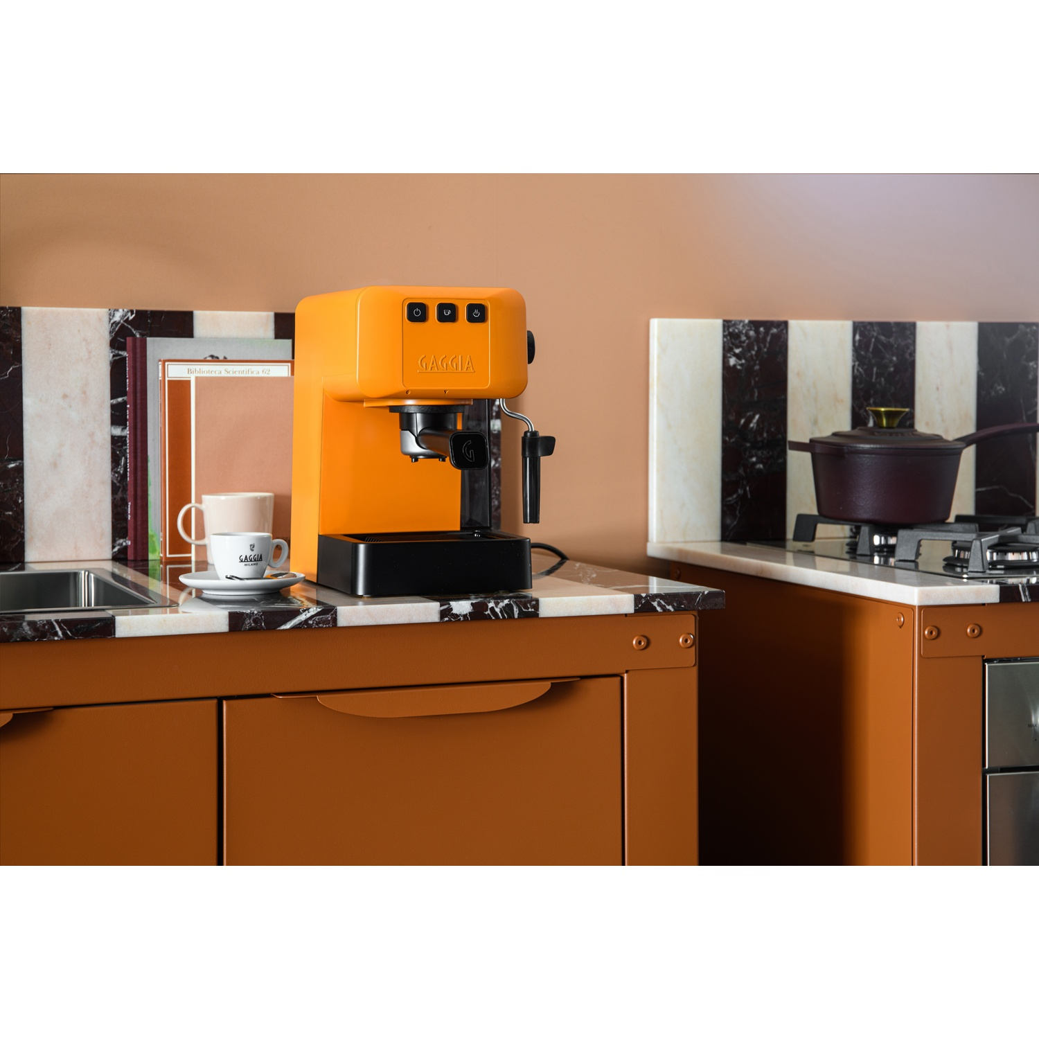 Una macchina per caffè espresso arancione è su un piano di lavoro in marmo accanto a una tazza di caffè.