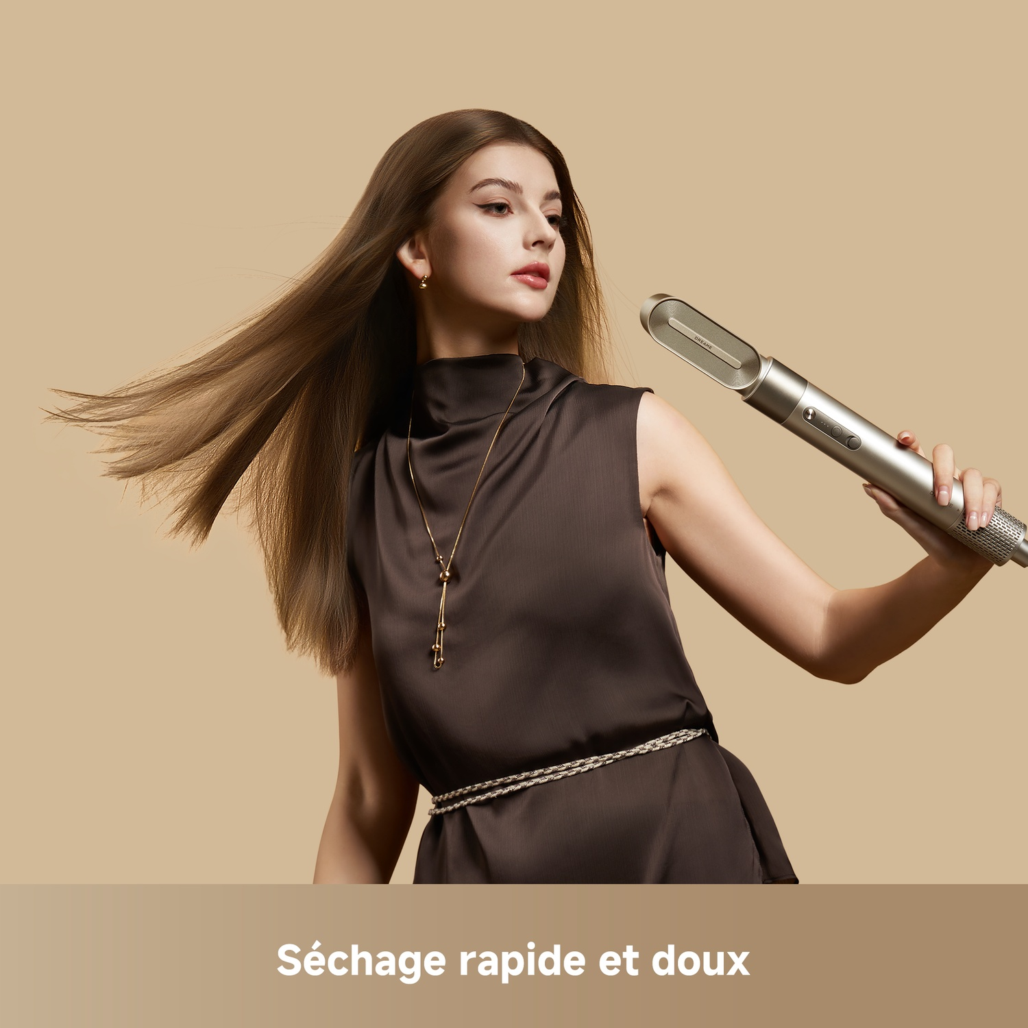 Femme aux cheveux bruns longs tient un sèche-cheveux argenté, robe avec ceinture.