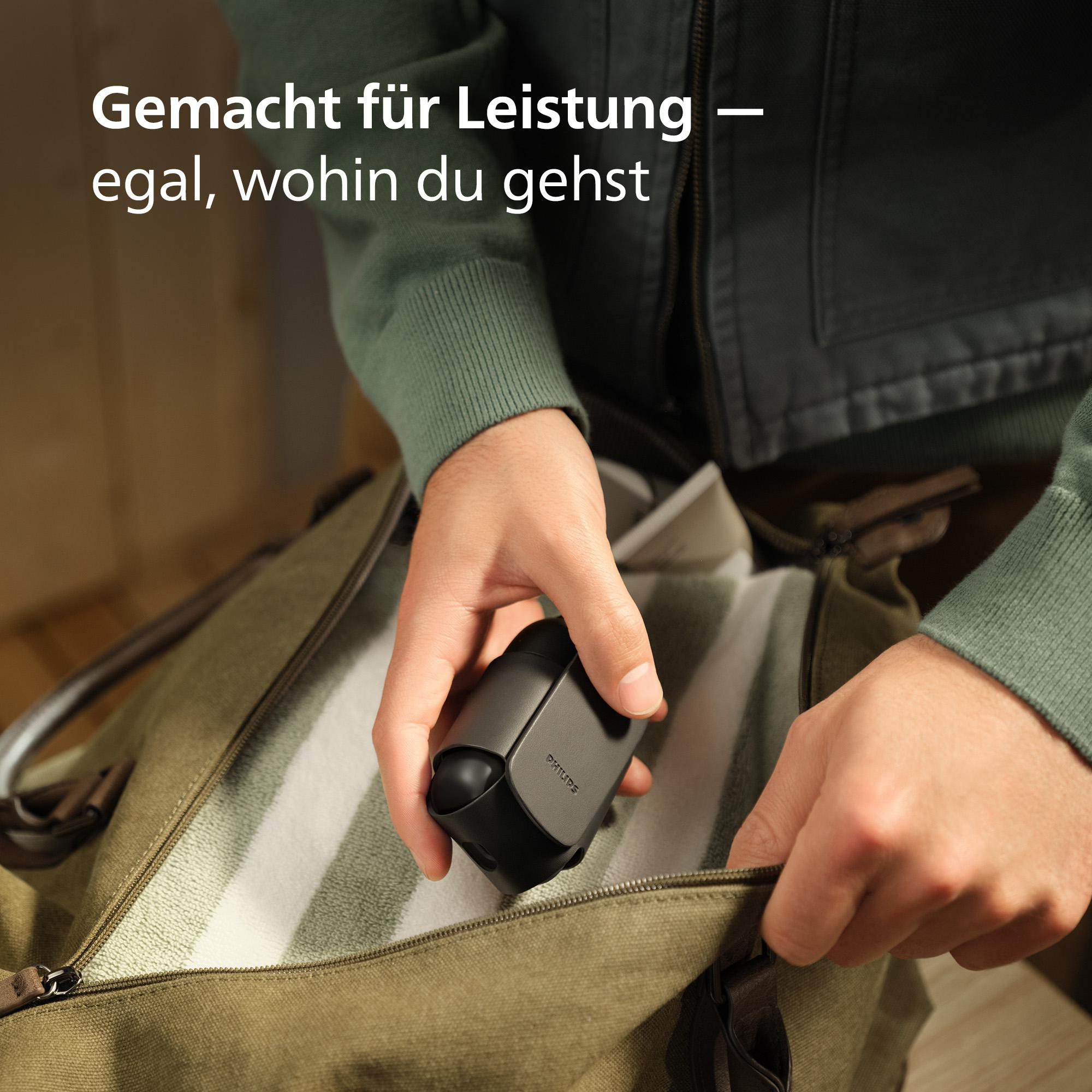 Eine Hand legt einen dunklen Philips-Rasierer in eine olivgrüne Tasche.