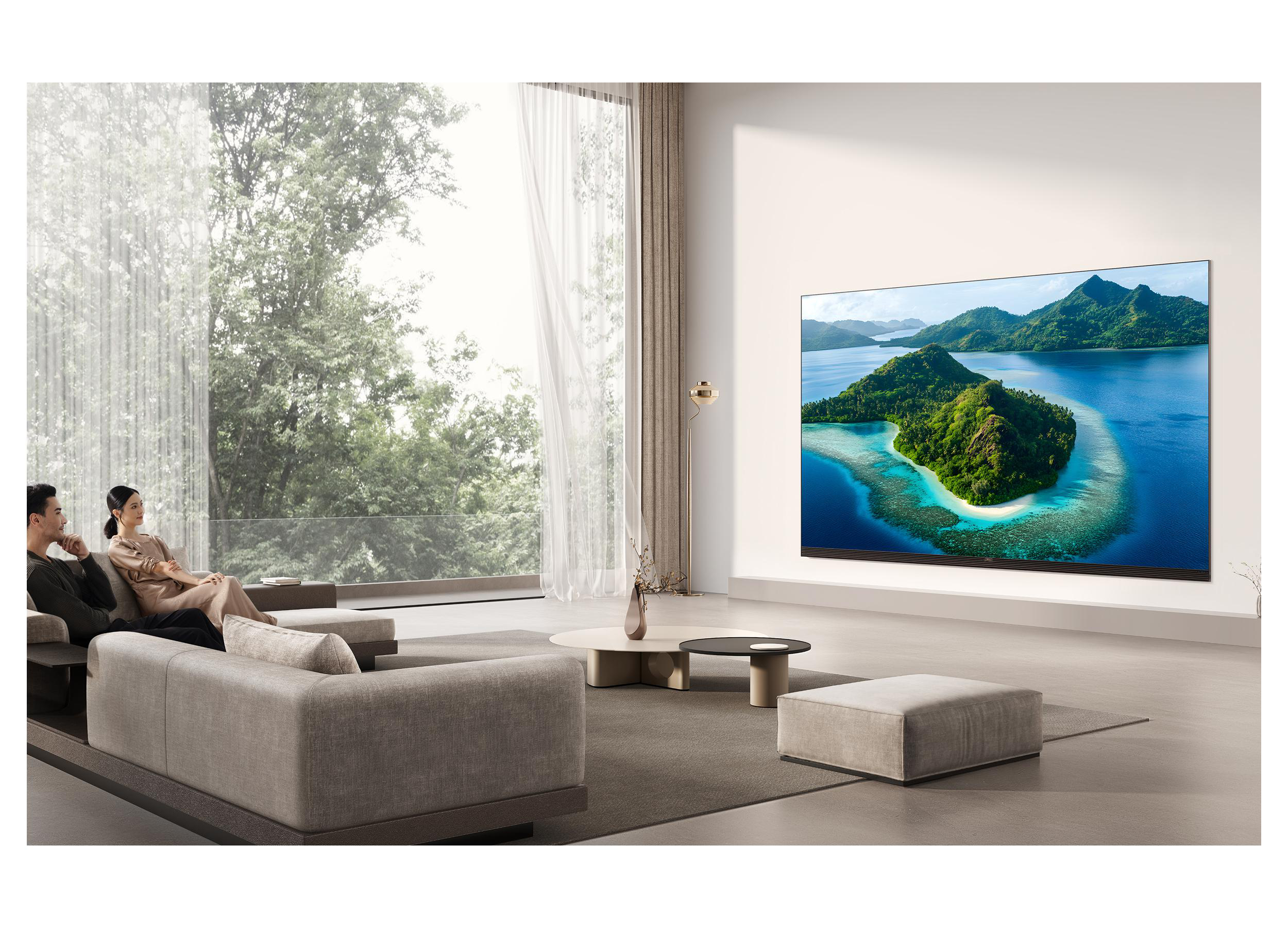 Ein Paar sitzt auf einem Sofa und blickt auf einen großen Fernseher mit tropischer Inselansicht.