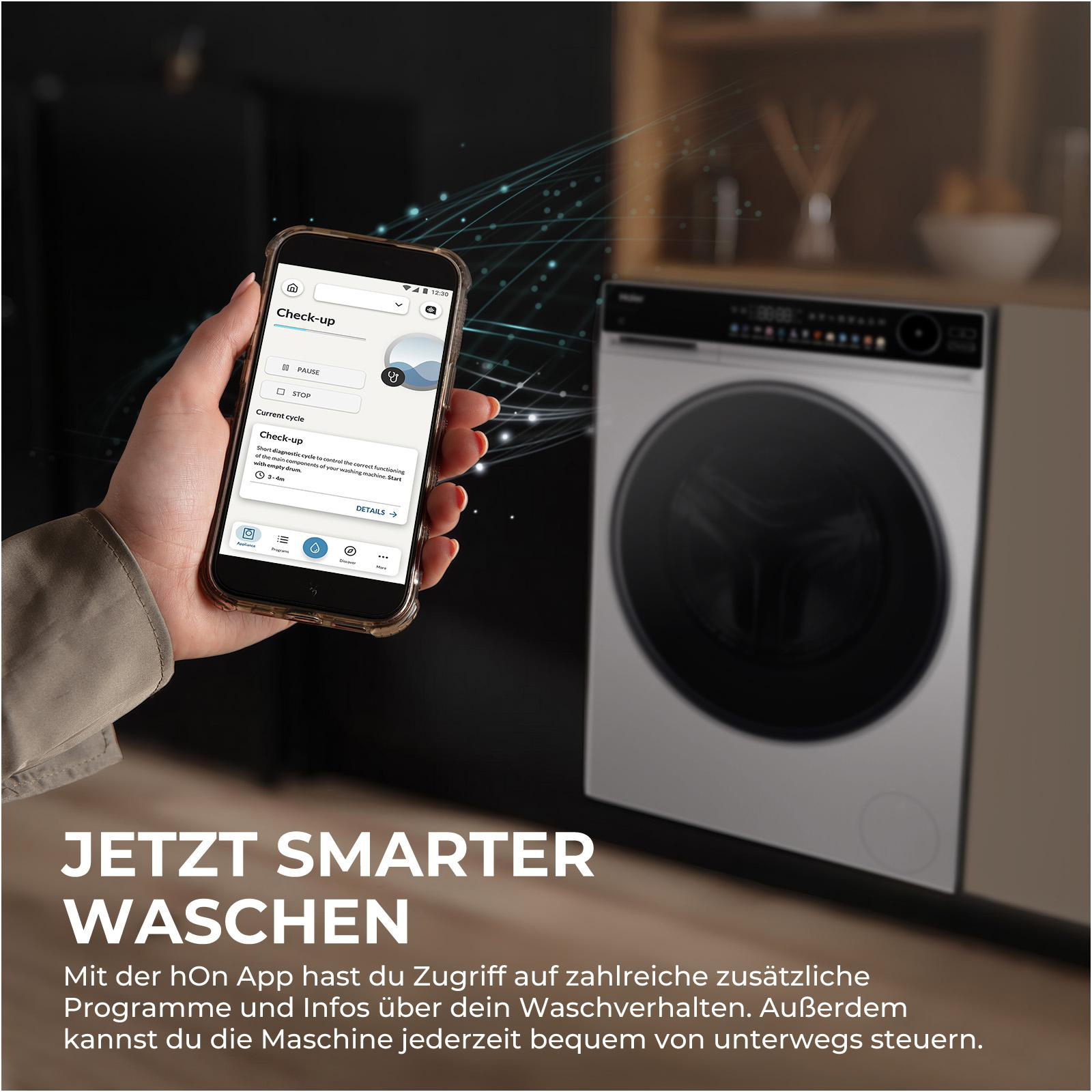 Eine Hand hält ein Smartphone mit einer Waschmaschinen-App. Daneben steht eine Waschmaschine.