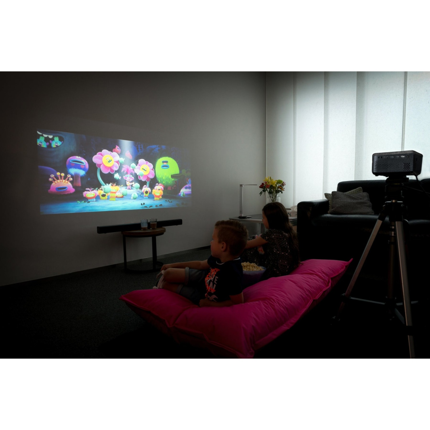 Deux enfants assis sur un pouf rose regardent un film projeté sur le mur.