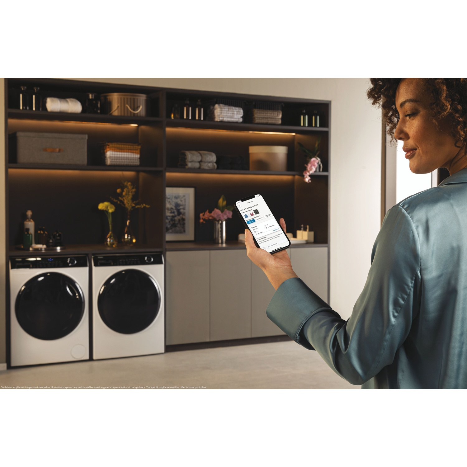 Een vrouw houdt een smartphone met een was-app vast voor planken met wasmachines.