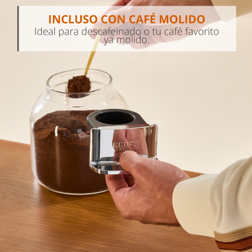 Una mano sostiene un portafiltro de café plateado delante de un frasco de café molido.