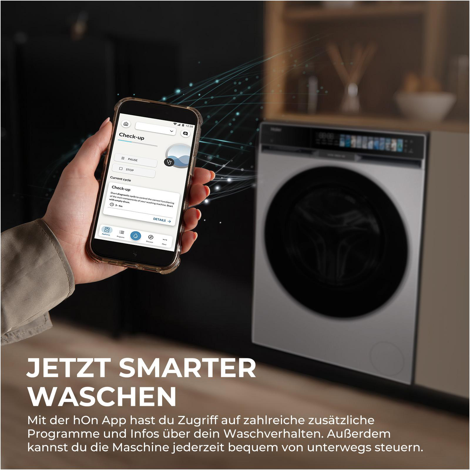 Eine Hand hält ein Smartphone mit einer Waschmaschinen-App. Im Hintergrund eine Waschmaschine.