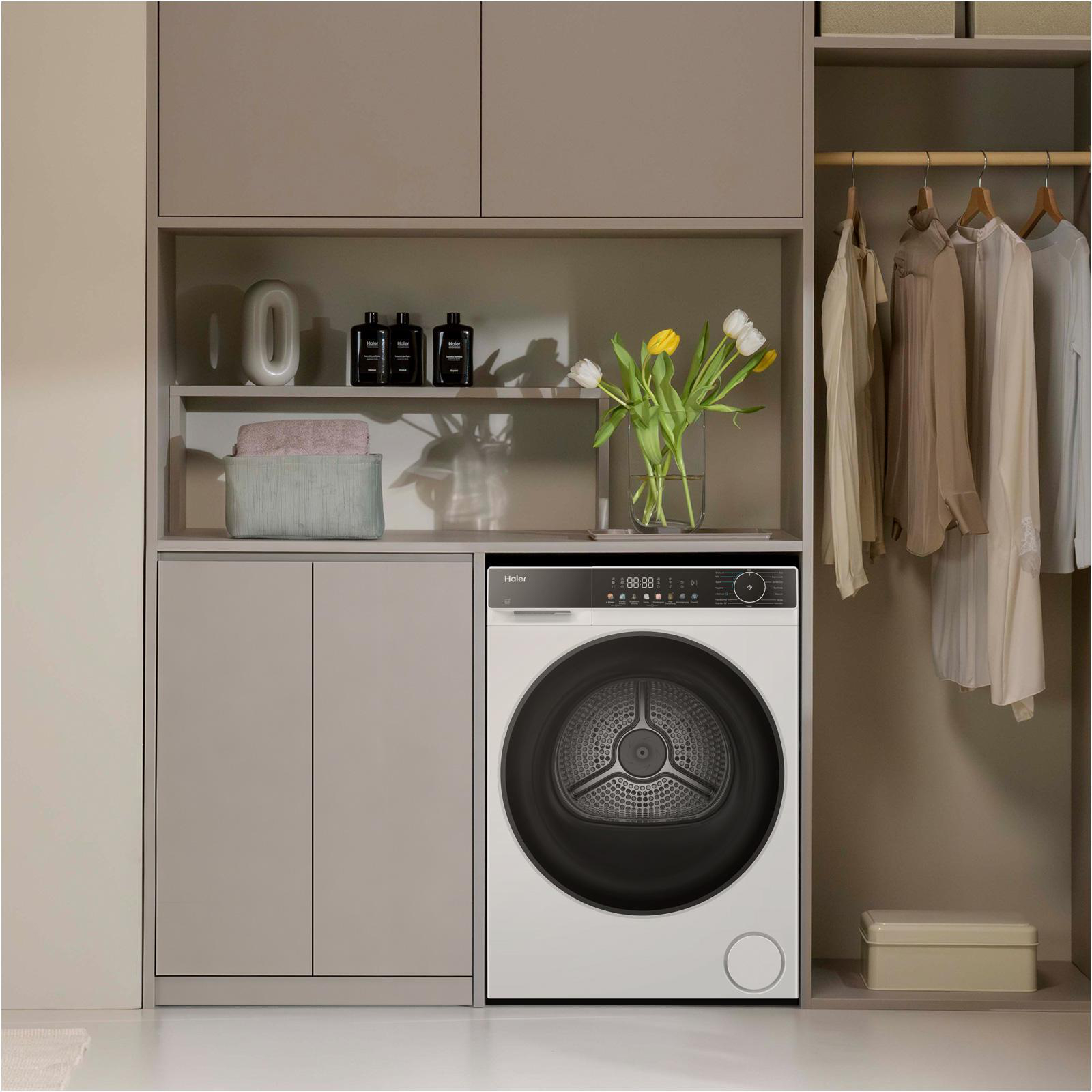 Eine weiße Waschmaschine steht neben einem Schrank mit Kleidung. Tulpen stehen in einer Vase.