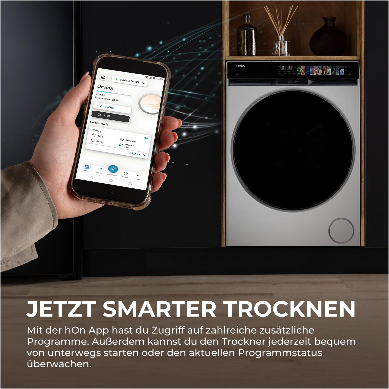 Eine Hand hält ein Smartphone mit einer Wäschetrockner-App. Daneben steht ein Haier-Trockner.
