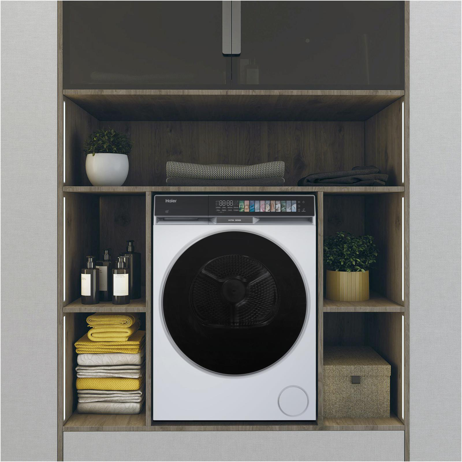 Ein weißer Haier-Trockner steht mittig auf einem Regal, umgeben von gefalteten Handtüchern, Flaschen, Pflanzen und einer Aufbewahrungsbox.